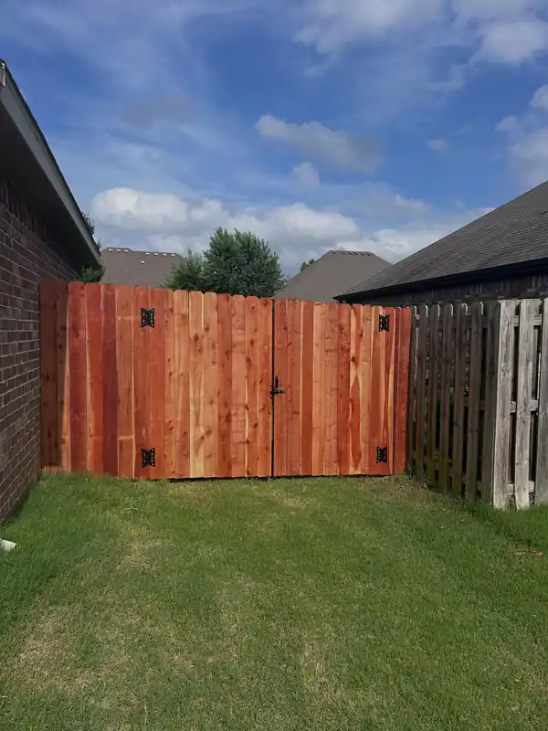 Stained red-cedar double gate between a brick wall and an older shadowbox fence, green lawn in front