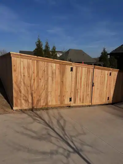 Cedar enclosure with a walk gate on a concrete pad, a dumpster or equipment screen