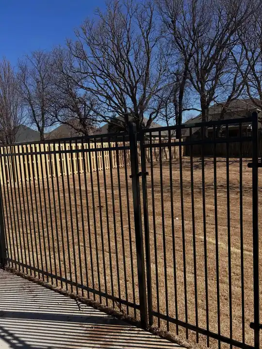 Black aluminum fence with a double gate on a wooded lot