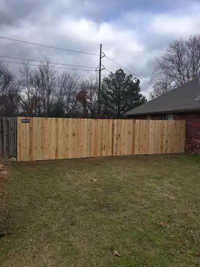 Pressure-treated pine privacy fence run behind a brick house on an overcast day