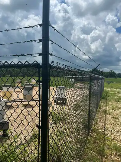 Close view of the barbed-wire top and a corner post on the bee yard fence
