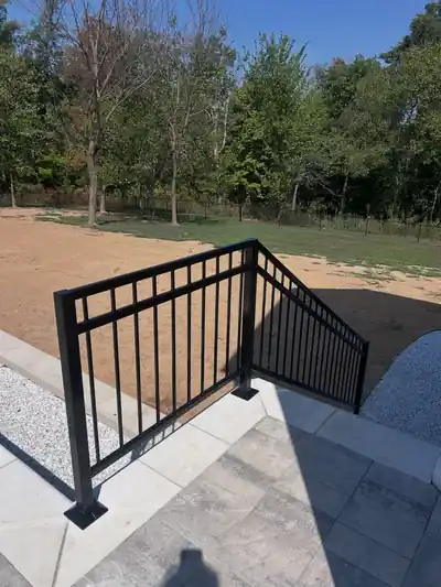 Black aluminum stair railing on new concrete steps in a fresh dirt yard