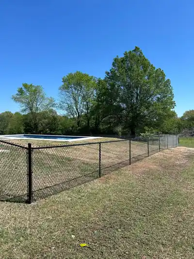 Black chain link fence along a pool yard with trees behind