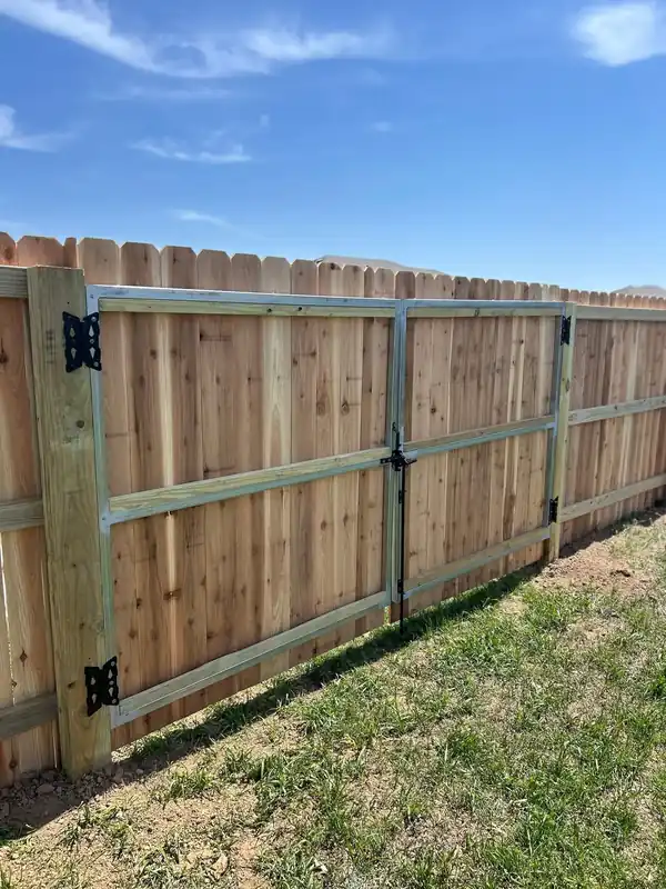 Cedar privacy fence with a galvanized steel-framed double gate and black hinges, built by Fence Pros NWA