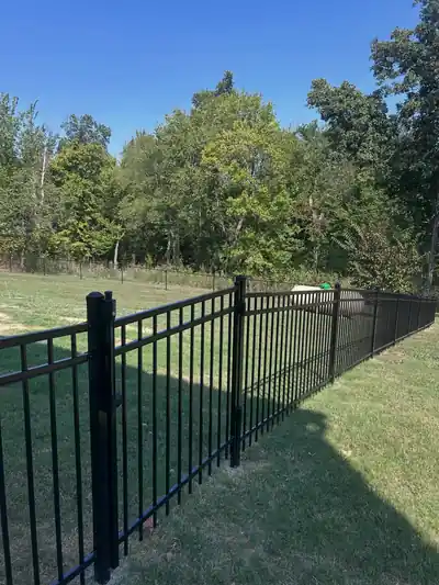 Black aluminum fence along a mown lawn at a tree line