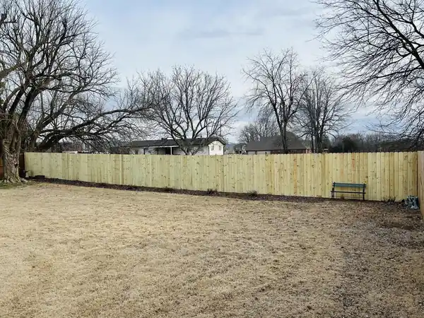 A long pine privacy fence run across a wide backyard with bare winter trees behind, built by Fence Pros NWA