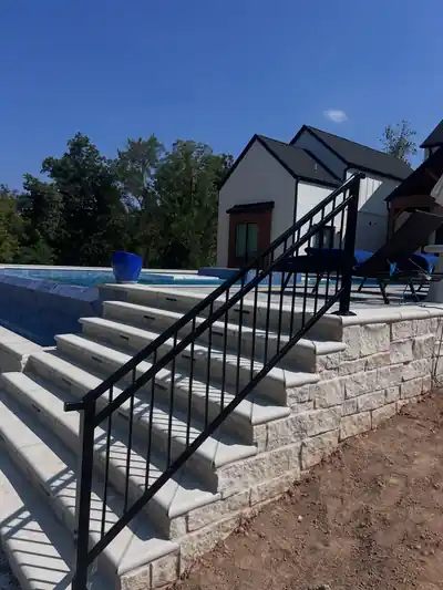 Black aluminum stair railing up stone steps to a pool deck