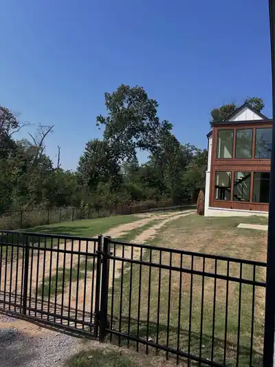 Black aluminum fence and gate across a gravel drive, house with a glass sunroom behind