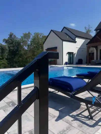 Black aluminum railing at a pool edge with a lounge chair and a modern white house behind