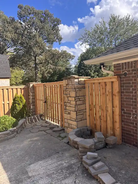 Cedar shadowbox fence and gate meeting a stacked-stone pillar beside a brick house
