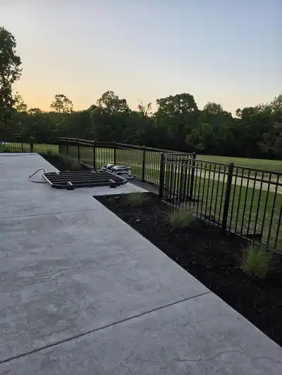 Black aluminum fence along a new concrete patio at dusk